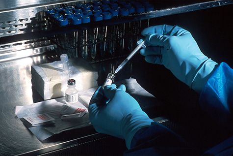 A lab technician, wearing gloves using syringes and tubes